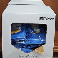 Large white cardboard box branded with 'Stryker', partially open showing multiple blue sealed packs of bath cloths inside.