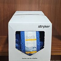 Box containing multiple packs of Stryker Sage Comfort Bath hygienic washcloths with branding visible.