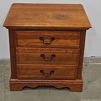 Front view of solid oak nightstand with 2 drawers closed, showing wood grain and black metal handles.