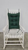 White wooden patio rocking chair front view with green cushioned back and seat pads.