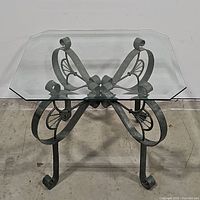 Glass top side table showing metal butterfly base design from a frontal angle.