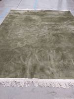 Full view of the 9x12 olive green velvet area rug laid flat on a concrete floor showing the embossed floral design and fringed edges.