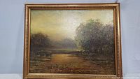 Full view of framed painting depicting swamp or marsh with water and trees in green and gold tones.