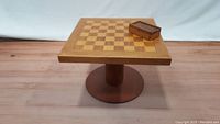 Full view of the wooden chess table showing the inlaid chessboard surface and the wooden box with checkers pieces on top.