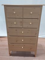 Front view of a tall pine dresser chest with 5 drawers and wooden knobs.