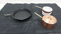 Cast iron skillet on left and copper with white ceramic double boiler pieces on right.