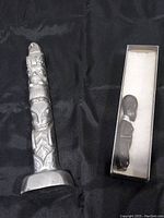 Aluminum Native American Inuit totem pole alongside boxed wooden tribal woman bust on black fabric background