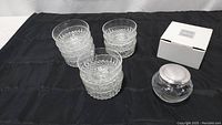 Three stacks of 10 clear glass bowls with a diamond pattern alongside a Mikasa crystal bowl in its box on a black cloth.