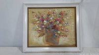 Full view of floral still life oil painting in white wooden frame against white background