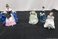 Full view of all 4 Royal Doulton Victorian ladies figurines arranged in a row on black cloth background.