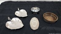 Overview of all five silver items on a black cloth background: two silver leaf dishes, oval platter, Paul Revere bowl, and sterling silver plate.