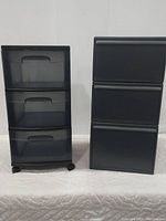 Both storage drawer units shown side by side on white backdrop. Left unit is clear plastic with black framing and wheels; right unit is all black stackable without wheels.