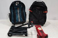 AOKING laptop backpack front view with multiple compartments and zipper pulls visible, stacked next to black and red folding carts.