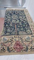Full view of tapestry laid flat showing entire Tree of Life design and floral border with rod alongside.