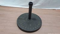 Black resin patio umbrella stand shown from side angle, displaying round base and central pole holder