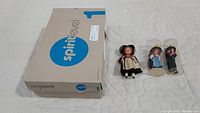 Three vintage dolls displayed alongside original Spirit Level box, two dolls in clear plastic display tubes, one loose doll in traditional dress.