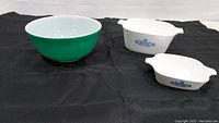 Pyrex mixing bowl and 2 CorningWare dishes displayed on black cloth, showing full contents of lot.