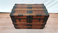 Front angled view of antique wooden steamer trunk showing wood and metal band construction, lock and latches on front panel.