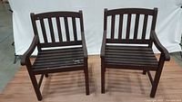Pair of dark brown wooden outdoor chairs side by side, showing front view with peeling paint on the seats.