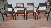 Four wooden outdoor arm chairs shown in a row. All similar design with horizontal slat backs and seats, medium brown wood, armrests curved outward.