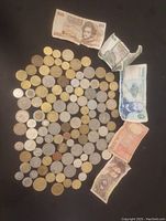 Wide view showing an assortment of foreign coins and five different foreign bills spread on a dark surface.