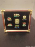 Framed John Deere enamel pin collection with seven tractor model pins and a central logo pin presented on a black velvet background.