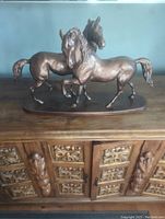 Front view of bronze-colored horse sculpture showing two horses side by side on an ornate wooden surface.