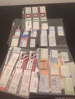 Photo showing an assortment of ticket stubs from various sports and concerts, organized in plastic sheets on a black surface.
