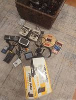 Overview of all items including various electronics, cameras, controllers, headphones, and a wicker basket on the floor