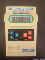 Front view of vintage handheld electronic football game with field graphic, control buttons, and speaker grille.