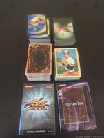 Top view of multiple card stacks including Duel Masters, Yu-Gi-Oh, Topps baseball cards, and rulebooks