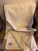 Full view of the cream wool blanket draped over a chair showing fabric texture and blanket stitch edges.