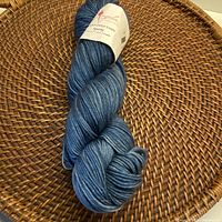 Full skein of blue Anzula Squishy yarn laid on woven surface showing the twisted yarn and color variations.