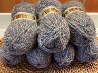 7 balls of Sirdar Tweed wool yarn stacked in two rows, showing labels and color specks