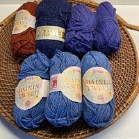 Overall image of the 7 balls of yarn placed in a wicker basket showing the variety of colors and brands.