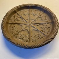 Top view of round ceramic cookie mould with 8 heart and foliage embossed sections and decorative rim.