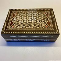 Top view of the wooden box showing intricate geometric inlaid pattern with stars and triangles in natural wood, black, white and red colors.