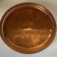Top view of the large round solid copper tray showing embossed leafy swirl design and textured rope edge with cut-out sides.