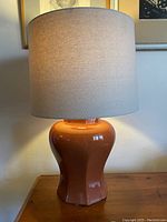 Full view of the ceramic lamp with new neutral fabric lampshade on wooden surface near the wall.