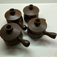 Set of four chocolate brown lidded bowls by Denby showing side handles and lids, matte finish with linear details.