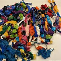 Over 150 skeins of embroidery thread in various colors including blue, green, orange, pink, purple, white, black, and yellow arranged loosely.