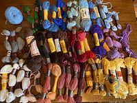 Top-down photo showing a diverse and colorful collection of over 50 skeins of wool tapestry yarn arranged in rows with visible labels.