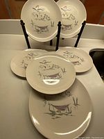 Set of 6 Royal Doulton plates with Venetian scenes arranged on a countertop and standing rack.