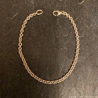 Full view of sterling silver chain bracelet laid flat showing the round solid links and lobster clasp.