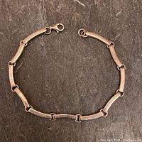 Full view of the sterling silver Fossil bracelet laid flat, showing curved square bar links connected by circular links with lobster clasp closure.