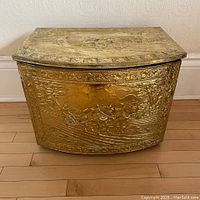 Front view showing repousse brass with horses and carriage scene, leafy border and curved front panel