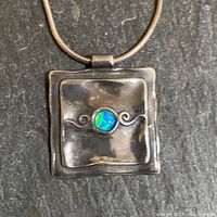 Close-up of square sterling silver pendant with blue-green opal center mounted on silver snake chain