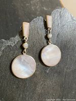 Pair of vintage sterling silver mother of pearl pierced earrings displayed on a textured dark stone surface, showing full front view.