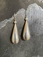Pair of vintage sterling silver teardrop-shaped earrings displayed on dark textured background showing overall shape and length.