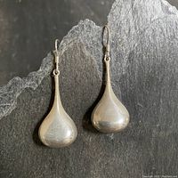 Full view of the pair of silver teardrop dangle earrings on black textured background.